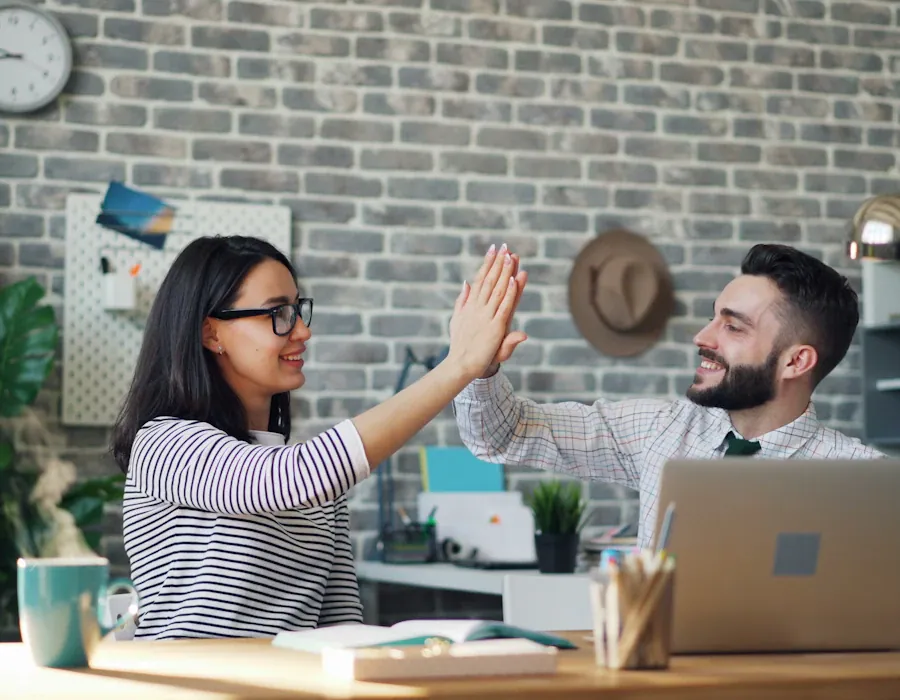Two colleagues high-fiving at a laptop